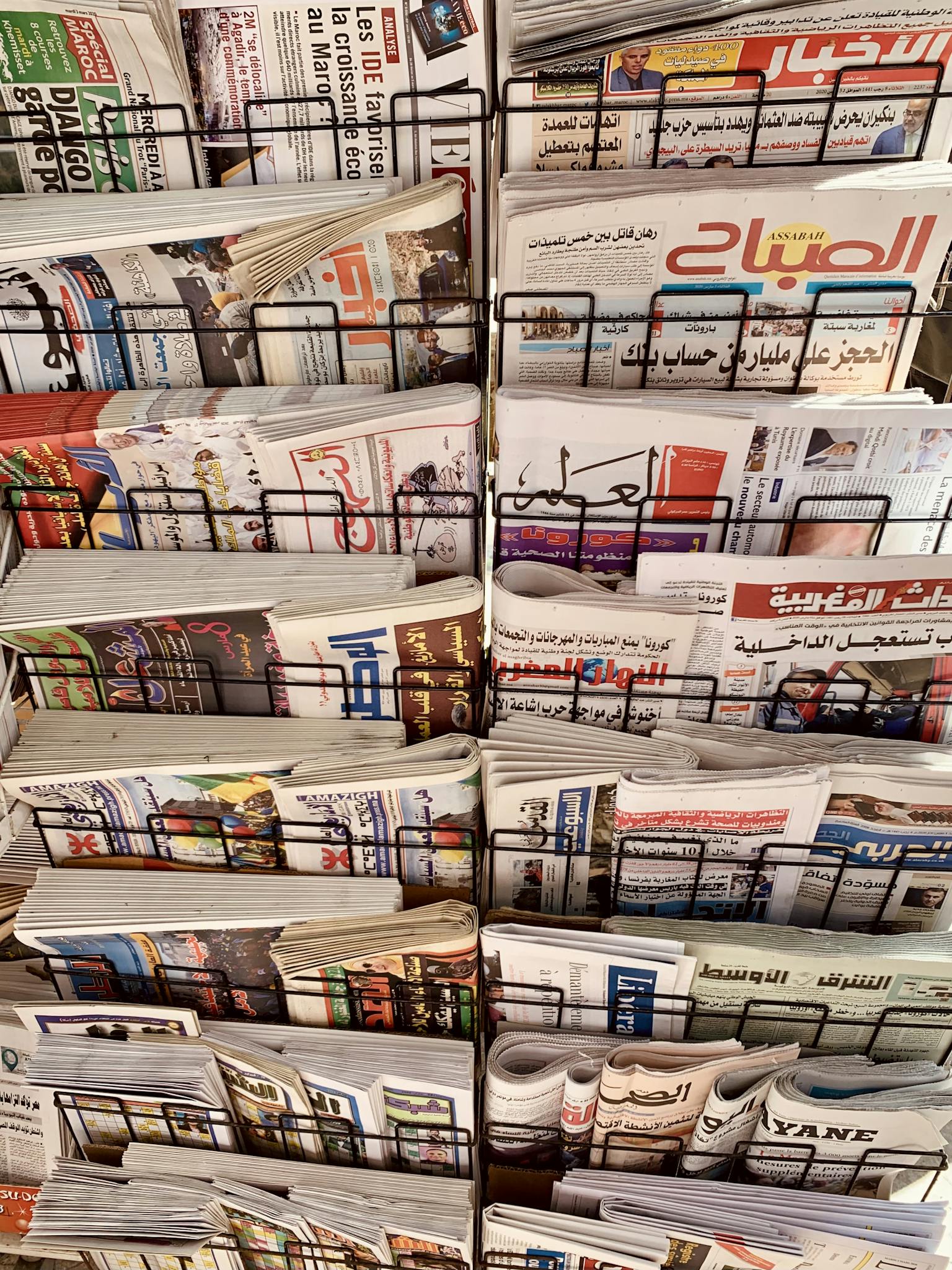 A diverse collection of newspapers in various languages displayed on a metal stand.
