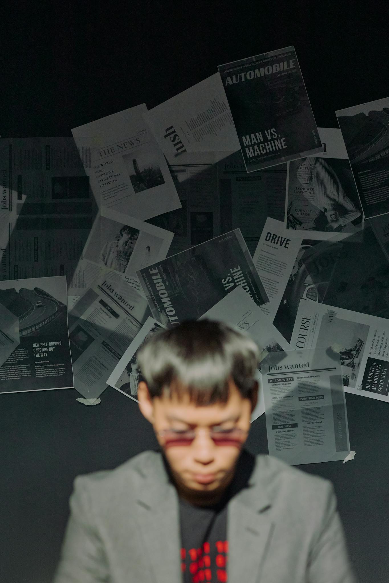 A focused man in a modern setting with newspaper clippings on the wall behind him.