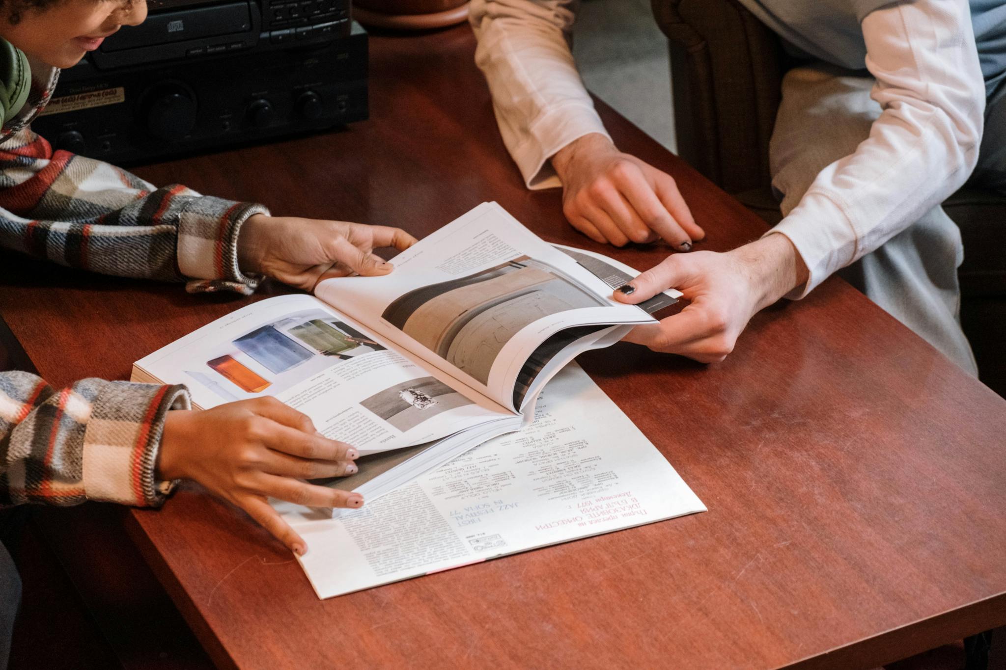 Two individuals reviewing a magazine on a wooden table indoors.